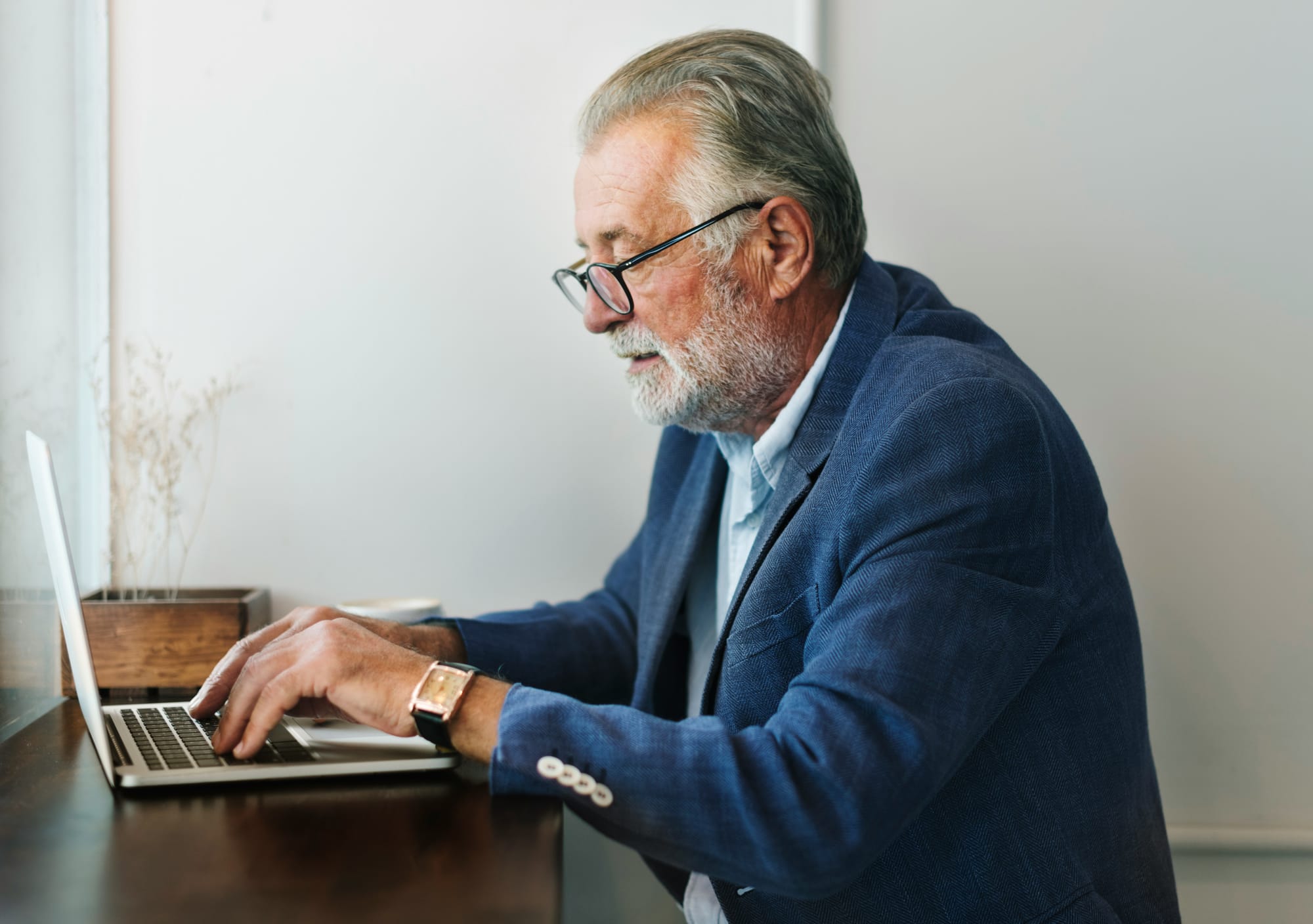 A well-dressed and elegand senior gentelman is working on a laptop.